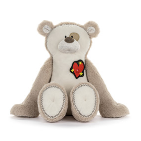 Front view of a grey and white teddy bear. The bear wears a small heart badge on the right side of its chest.