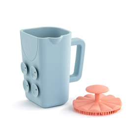 Front view of a blue bath cup and pink brush set. The cup is turned so the handle is on the right and suction cups are to the left. The brush is sitting to the right of the cup, bristle side down.