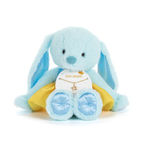 Front view of a plush blue bunny wearing a dark blue bodice and yellow tutu. The bunny has a necklace card on its lap, holding a gold necklace with a star charm. "You Shine!" is printed at the top of the card, above the necklace.