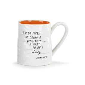 Front view of a white ceramic mug with orange interior, with the handle on the right. The mug's surface resembles a smoothed-out piece of crumpled notepaper. Text on the mug reads, "I'm so tired of being a person I want to be a dog".