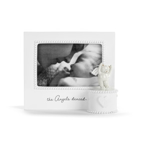 Front view of a white musical frame. The frame's opening has a white bead-like border. The music box mechanism is attached to the lower left corner of the front of the frame in a white circular box, and has a figure of a dancing teddy bear with angel wings on top and a heart in front. The phrase "The Angels Danced" is printed in black script under the frame's opening.