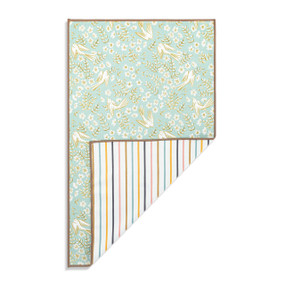 Top down view of a kitchen towel with a pattern of white birds and yellow flowers with green leaves on a sage green background on the front. The bottom right corner is folded up to show the back of the towel, which has a print of thin multicolored stripes on a white background.