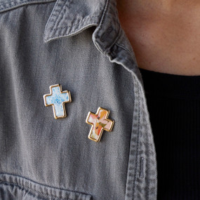 A person wearing a gray denim shirt wearing three colorful cross pins, two on the right shoulder and one on the left shoulder. .