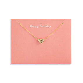 Top down view of a gold necklace with a heart charm attached to a coral pink card. "Happy Birthday" is printed at the top of the card above the necklace.