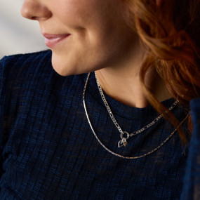 A woman wears a silver necklace with two layered chains.. The smaller chain is connected by a small charm with two hearts.