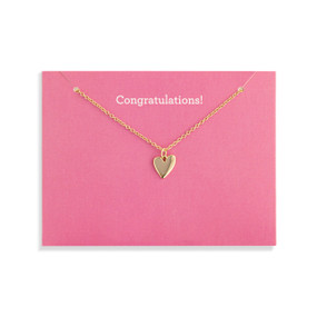 Top down view of a gold necklace with a gold heart charm attached to a pink card. "Congratulations" is printed on the card above the necklace.