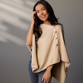 A woman wears a cream colored poncho with four brown buttons on the left side.