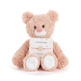 Front facing view of a pink teddy bear with a card on its lap. The card holds a pink ribbon bracelet with a daisy charm. "Flower girl" is printed on the card above the bracelet.