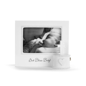 Front view of a white musical frame. The frame's opening has a white bead-like border. The music box mechanism is attached to the lower left corner of the front of the frame in a white circular box, and has a white cross on top and a heart with a cross at the center in front. The phrase "God Bless Baby" is printed in black script under the frame's opening.