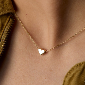 A woman wears a gold necklace with a small heart charm.