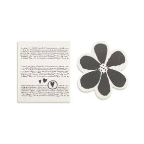 Top down view of a set of biodegradable dish towels set side by side. The towel on the right is shaped like a black daisy-like flower. The towel on the left is rectangular and has a print of tiny black hearts on a white background.