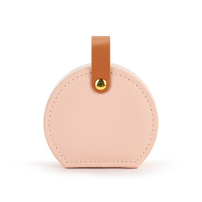 Front facing view of a circular pink traveling jewelry case. The brown strap is snapped at the top, holding the case closed.