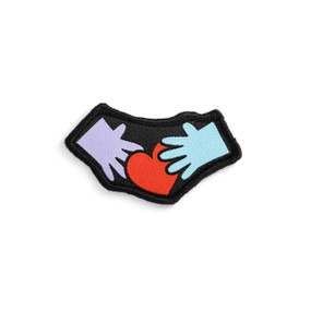 Front view of an irregularly shaped badge. The badge is a purple left hand and a blue right hand with a red heart between them. The badge can be attached to a Just Add Heart Bear.