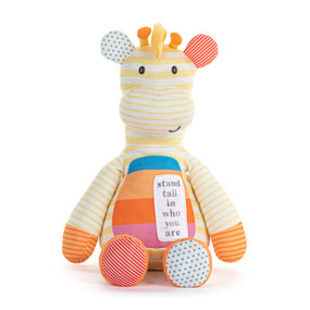 Front view of a plush giraffe. The giraffe's body is yellow and white striped. The chest is rainbow striped, with a patch on the left side that says "stand tall in who you are". The arms and legs are orange and white striped. The feet and ears are different colors and patterns.