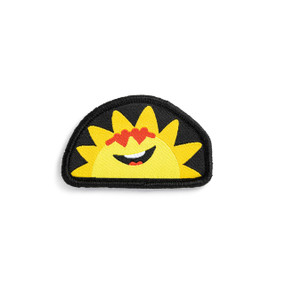 Front view of a semi-circular badge. The badge is a yellow sun with a smiley face and heart sunglasses on a black background. It can be attached to a Just Add Heart plush bear.