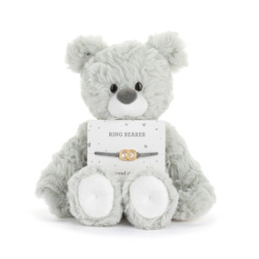 Front facing view of a gray teddy bear with a card on its lap. The card holds a dark gray cord bracelet with a charm made of two intertwined gold rings. "Ring Bearer" is printed on the card above the bracelet.