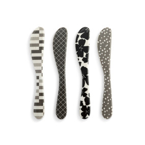 Top down view of a set of 4 melamine spreaders, set out side by side. Each spreader is a different color and pattern, unified with the colors black, white and gray.