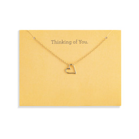 Top down view of a gold necklace with a floating heart charm attached to a yellow card. "Thinking of you" is printed at the top of the card above the necklace.