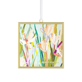 Front view of a glass suncatcher in a gold frame with a white cord threaded through a loop hanger on the top. On the surface of the glass is print of pink and orange flowers surrounded by green leaves. "Beautiful day" is printed on the lower left corner.