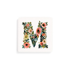 Front view of a square white coaster monogrammed with the letter M. The letter is former with a design of orange flowers and green leaves.