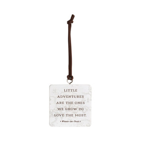 Left facing view of a white square hanging ornament. "Little adventures are the ones we grow to love the most - Winnie-the-Pooh" is printed over an illustration of the Hundred Aker Wood from the classic Winnie-the-Pooh stories.