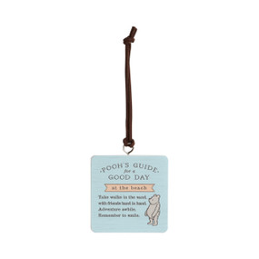 Front facing angled view of a light blue square hanging ornament with an illustration of classic Winnie-the-Pooh in the lower right corner. "Pooh's Guide for a good day at the beach. Take walks in the sand with friends hand in hand. Adventure awhile. Remember to smile." is printed across the middle.