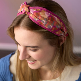 A young woman wears a pink and gold floral print fabric headband with a knot slightly off center at the top.