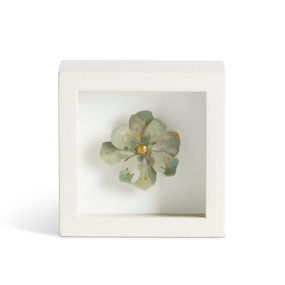 Front facing view of a white square shadow box. At the center of the box is a sculpture of a single light green flower.