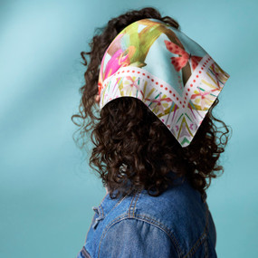 A woman standing with her back to the viewer wears a bandana scarf printed with flowers and butterflies tied over her hair.