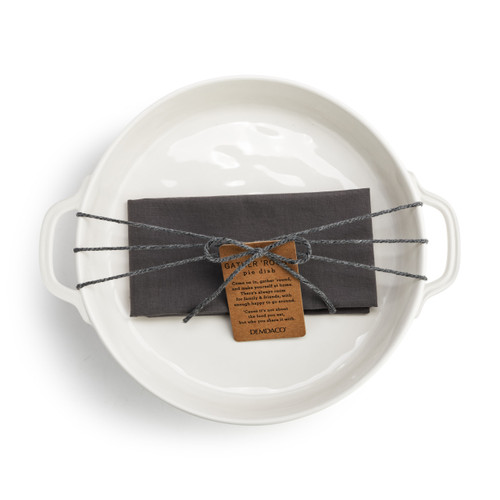 Top down view of a round white ceramic pie dish with a gray cloth inside, wrapped with cord and a product tag.
