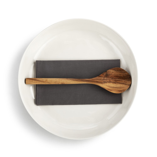 Top down view of a white ceramic serving bowl with a brown napkin and wood spoon inside.