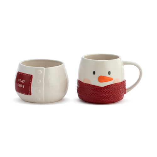 Front view of a white stoneware set of a bowl and mug shaped like a snowman wrapped in a red scarf. There is a red patch on the bowl that says "Stay Cozy".