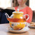 Close view of white/yellow/orange teapot on circle plate - blurred out image of woman reading in the back