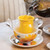 Close up of yellow/clear tea pot on a plate with silver water pourer