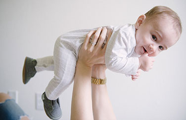 Adult hands holding an infant dressed in white in the air