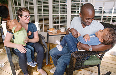 Mom and dad holding two young laughing children in their laps.