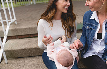 Two women playing with a baby in one of their laps. 