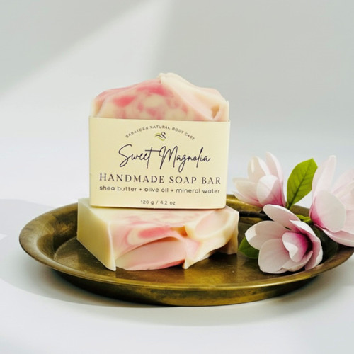 Sweet Magnolia handmade soap bar by Saratoga Natural Body Care, pink and cream artisan soap with floral swirls, shea butter and olive oil soap displayed with magnolia flowers