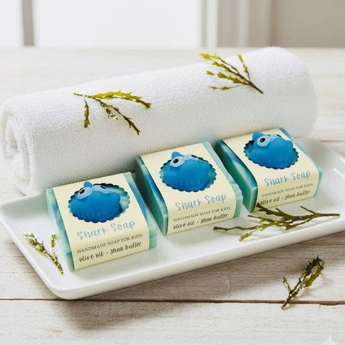 Handmade shark soap bars displayed on white tray with rolled towel, blue toy shark inside each soap, olive oil and shea butter soap.