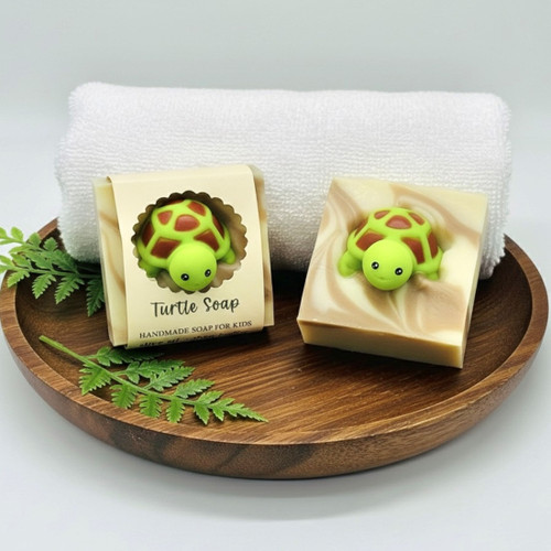 Handmade turtle soap displayed on wooden tray with fern and white towel — natural olive oil and shea butter bar with green turtle toy.