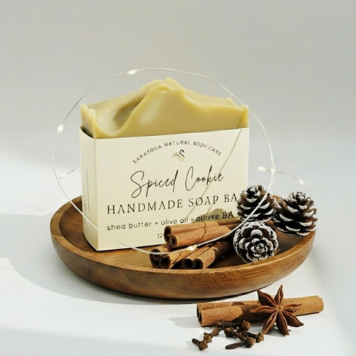Spiced Cookie handmade soap bar by Saratoga Natural Body Care on a wooden plate with cinnamon sticks, pinecones, and star anise. Warm, inviting holiday scent with creamy texture.