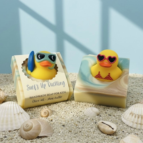 Handmade soap bars with cute beach-themed rubber duck toys, displayed on sand with seashells — Surf’s Up Duckling olive oil and shea butter soap.