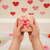 Kid holding a pink swirl handmade Valentine’s Day soap bar with a rubber duck toy over a bubble bath decorated with red and pink hearts.