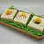 Sports-themed duck soaps unboxed and displayed in a wooden tray with green paper grass — handmade soap with basketball, baseball, and football duck toys.