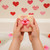 Kid holding a pink swirl handmade Valentine’s Day soap bar with a rubber duck toy over a bubble bath decorated with red and pink hearts.