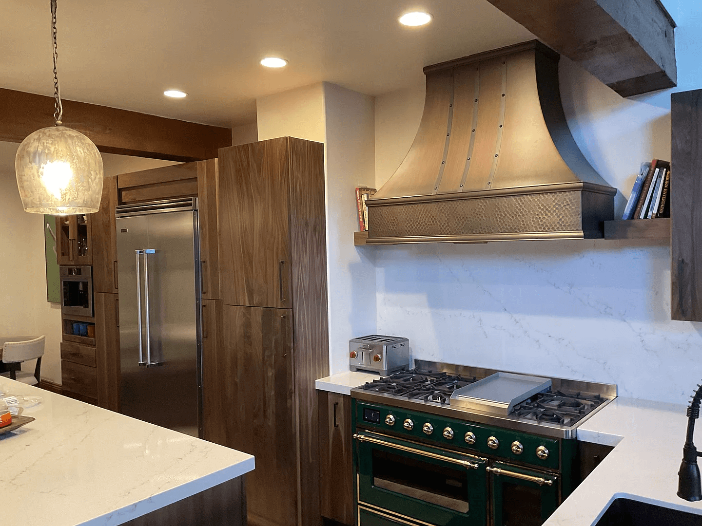 stainless steel custom range hood with brass trims in a white kitchen