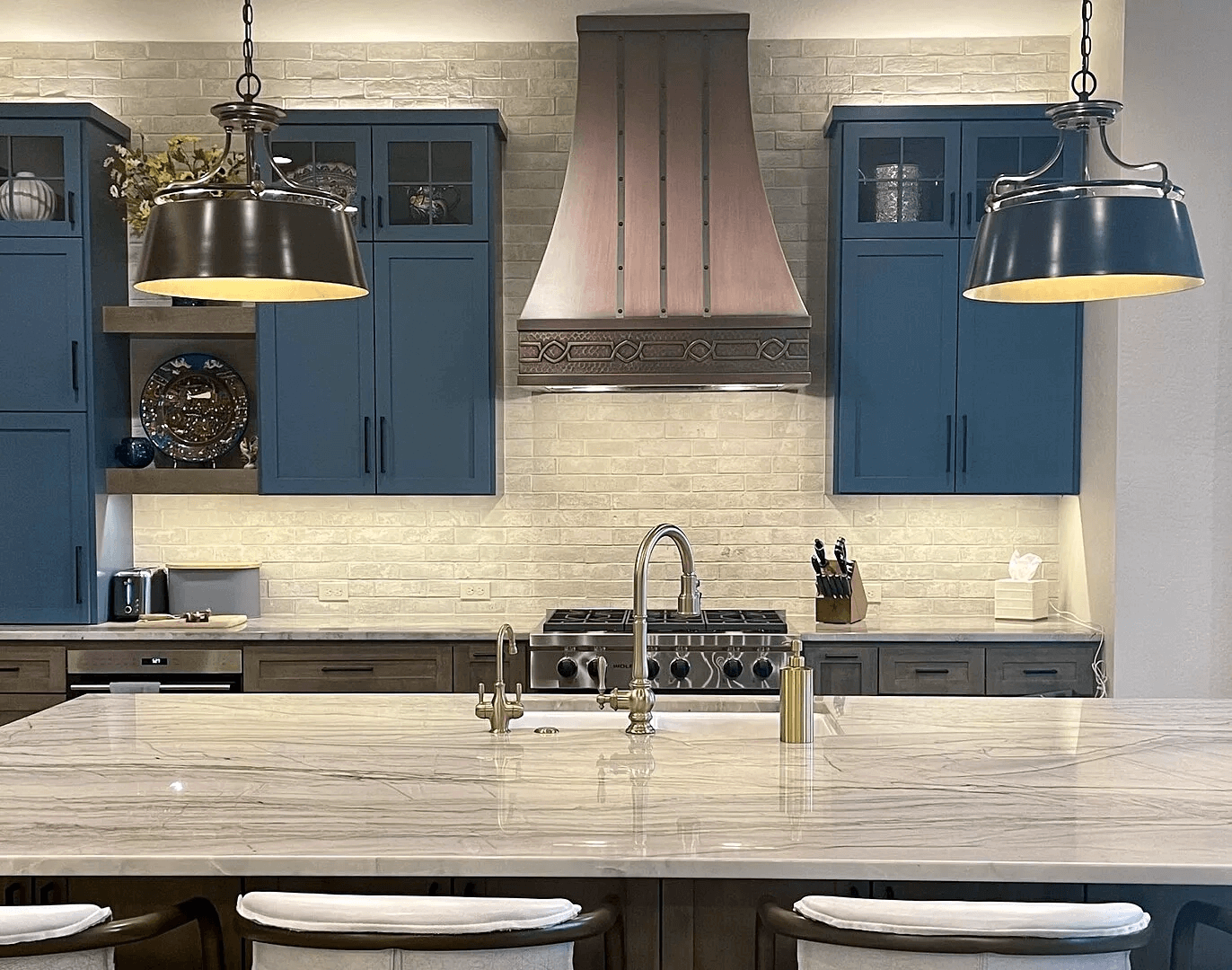 stainless steel custom range hood with brass trims in a white kitchen