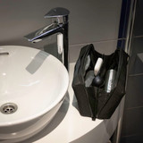 A black toiletry bag with various grooming items beside a white sink and chrome tap. The bag features a logo.