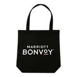 A black tote bag with handles, featuring a logo on the front, placed on a wooden table.