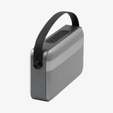 A wireless speaker in grey with a black handle and buttons on top, featuring a perforated speaker grille.
